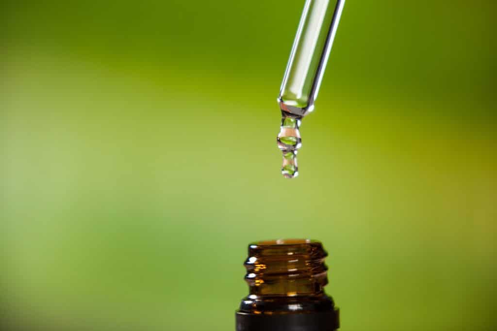 A pipette with a bead of water dangling from the end, ready to fall into the waiting  bottle below.