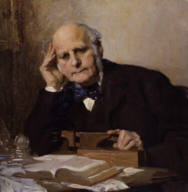 A painting of Sir Francis Galton, leaning with one elbow on a desk and his head resting on that hand. In his other he touches a wooden device, with an open book farther away on the desk. He wears a black suit and a bowtie, his grey hair framing his face (but bald on top)