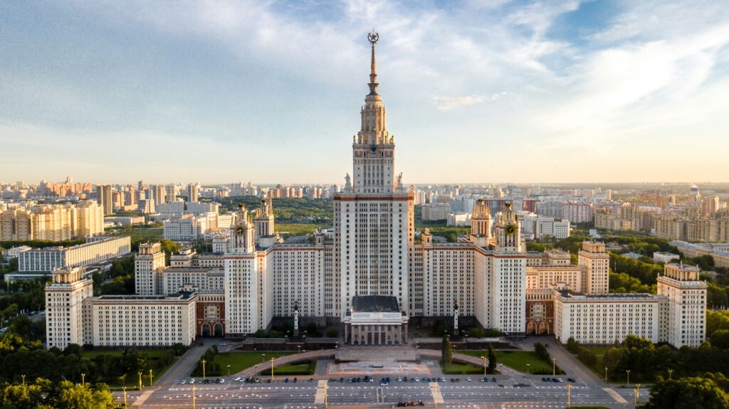 Moscow State University, a huge building, symmetrical with many windows, a spire rising atop its tall central tower. Gardens and pathways in front, and more of the city sprawling behind