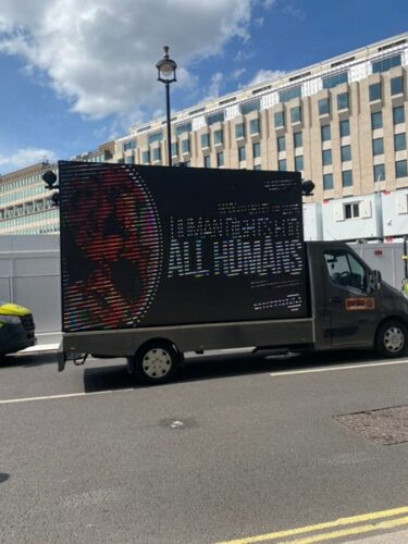 A digital pro-life sign on the back of a van driving along the street (text illegible except for 'Human rights... ALL HUMANS'