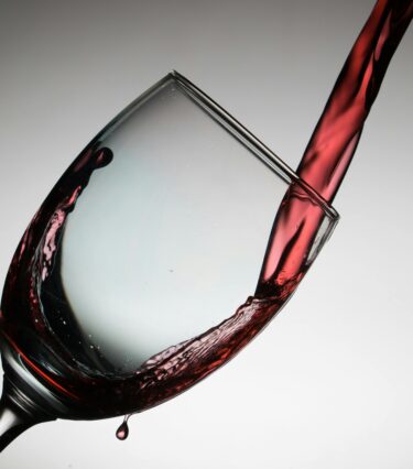 A wine glass being filled with red wine from a bottle which is out of shot