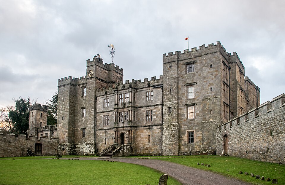 An exterior view of a large fortified manor house or castle with square four storey towers at each side of a three storey central area. The tops of the walls are crenellated.
