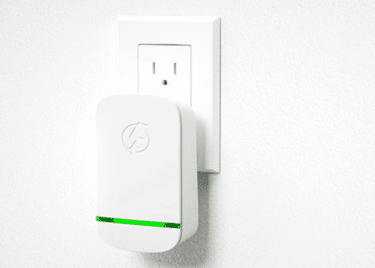 A white box measuring approximately 10cm tall and 5cm wide plugged into an electrical wall socket. The box has a green LED on the front.