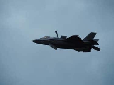 A flying aircraft against a dull, grey, cloudy sky - a USAF F35 strike fighter jet, features hard to pick out except for the cockpit as the material is all dark/black.