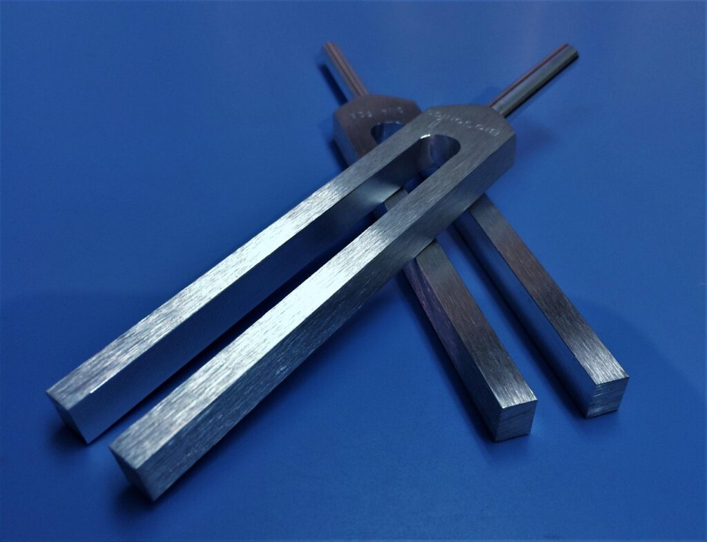 Two silver-metal tuning forks on a blue surface, one laid diagonally on top of the other