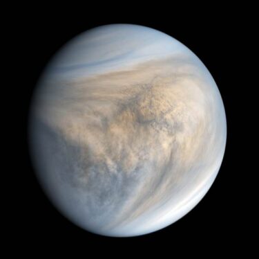 A photograph of Venus taken by the Akatsuki spacecraft. An almost-full gibbous Venus is bright against a solid black background. Swirling clouds cover the illuminated area, coloured white or grey near both poles and pale yellow, brown, and grey elsewhere.