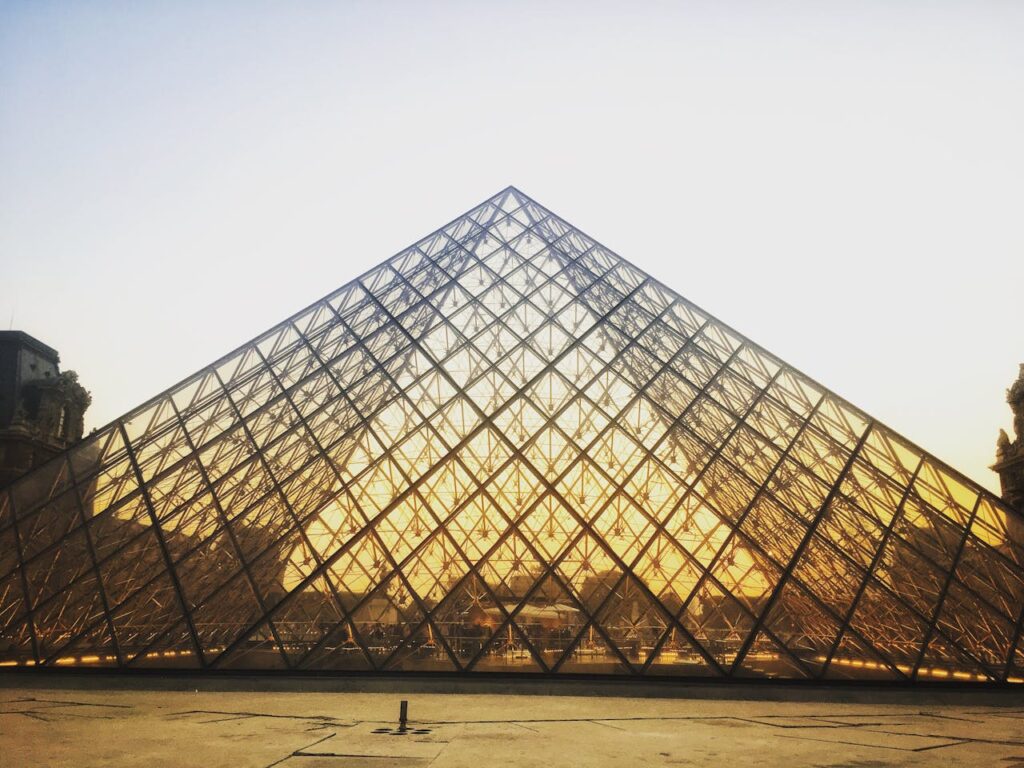 A photograph of the pyramid at the Louvre in Paris. Golden sunlight shines through the glass structure, showing the supporting steel lattice.