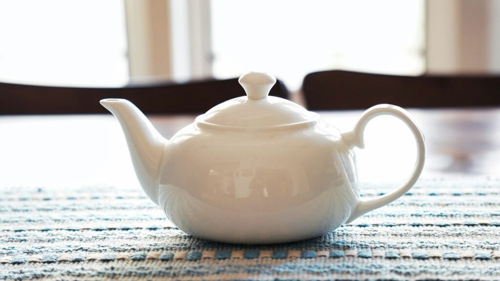 A closeup photograph of a white teapot on a table.