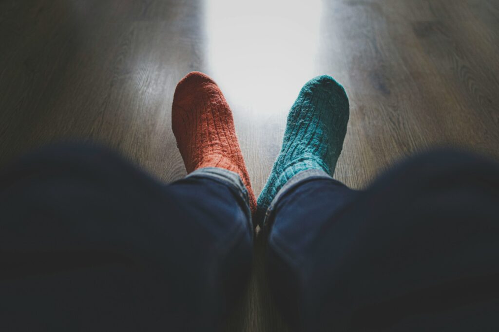 A photograph showing a person's legs from the knees down. They are wearing dark denim jeans, and odd woollen socks; the left one orange and the right one pale blue.