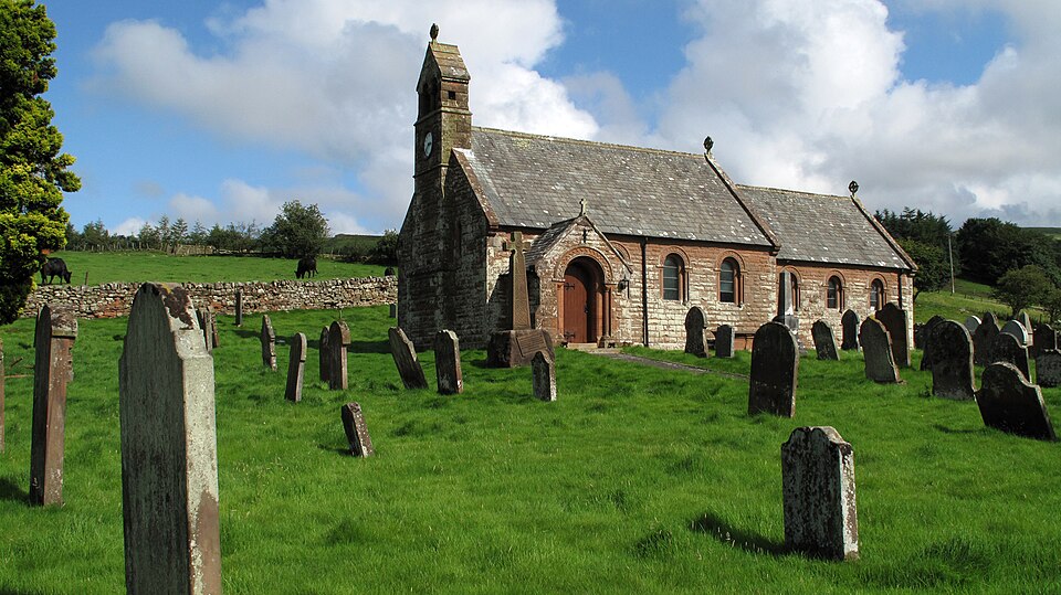A small stone church, lacking tower or steeple. It is set in a grass churchyard containing headstones, surrounded by a dry stone wall.