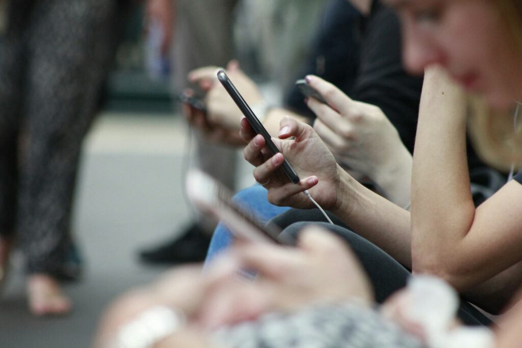 A photograph showing several seated people, holding smartphones on which they appear to be scrolling on the screens.