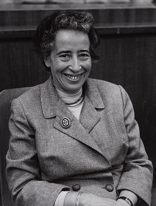 Black and white photograph of a smiling middle-aged woman with curly hair, wearing a twill jacket with a brooch on the right lapel.