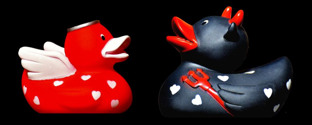 Two rubber ducks facing each other against a completely black background. The left duck is a red 'angel' with wings and a silver halo. The right is a black 'devil' with red horns, bill and a trident. 
