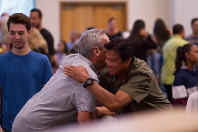 Two men hug, amid groups of other people talking.