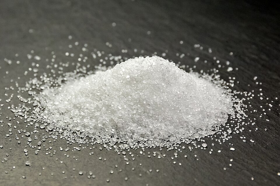 A pile of white grainy substance, resembling sugar, on a dark surface