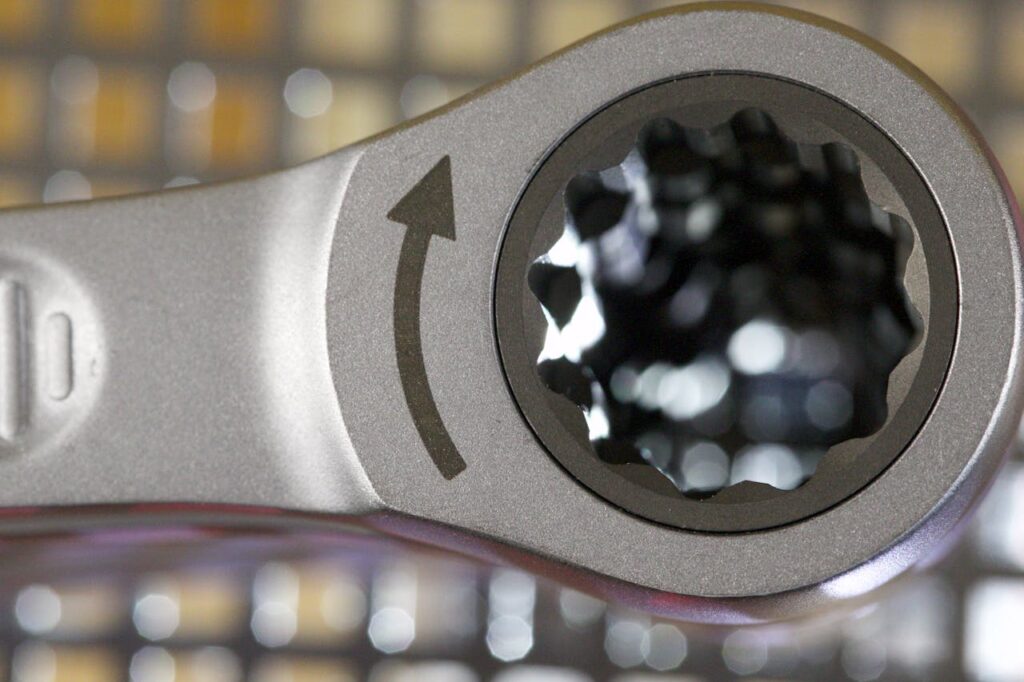 A closeup photograph of the head of a ratchet wrench, with a clockwise arrow marked on it.