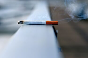 A lit cigarette lying on a surface, producing faint curls of smoke