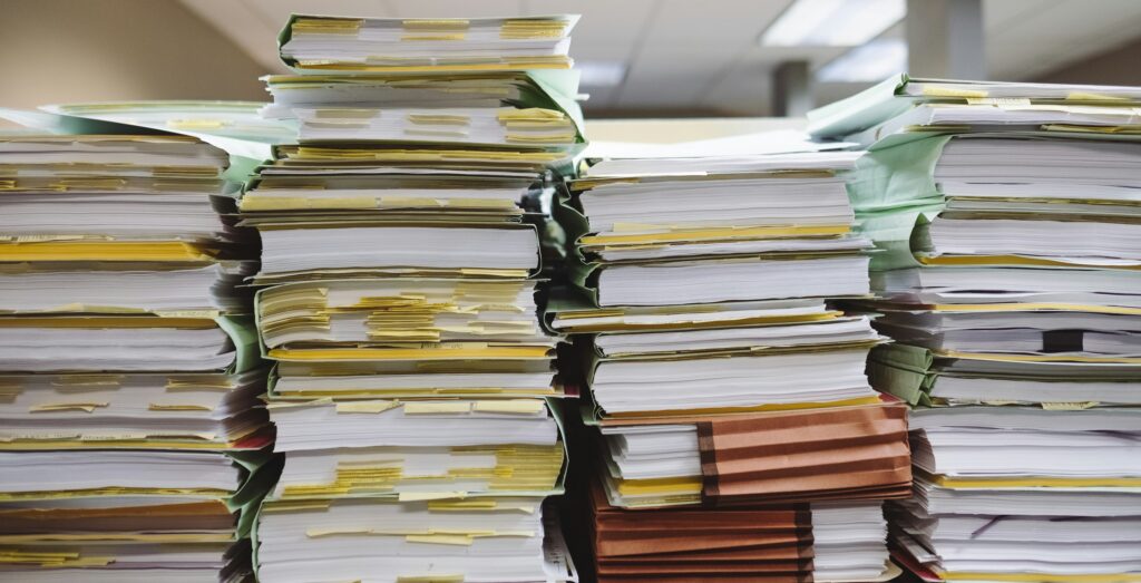 Several vertical stacks of books, with many pages marked by yellow post-it notes, and cardboard folders full of papers, in a typical-looking office room