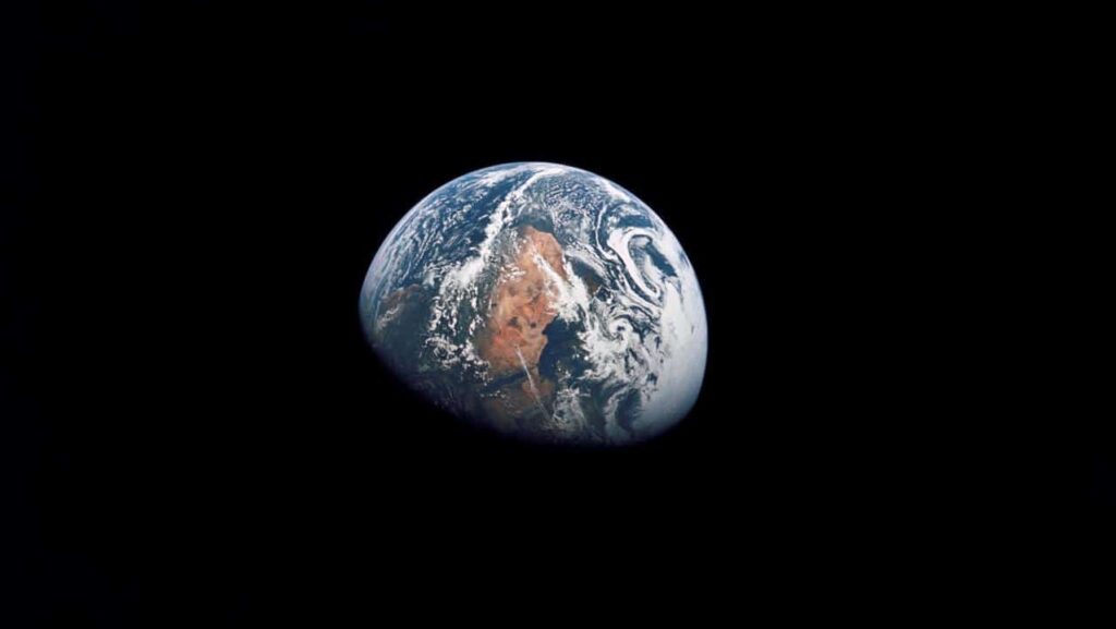 Photograph of a gibbous Earth against the blackness of space. Visible is the white arctic region, a mostly white cloud-covered Europe, the Mediterranean Sea, a reddish-brown north Africa and Arabia, and a greener Africa south of the Sahara.