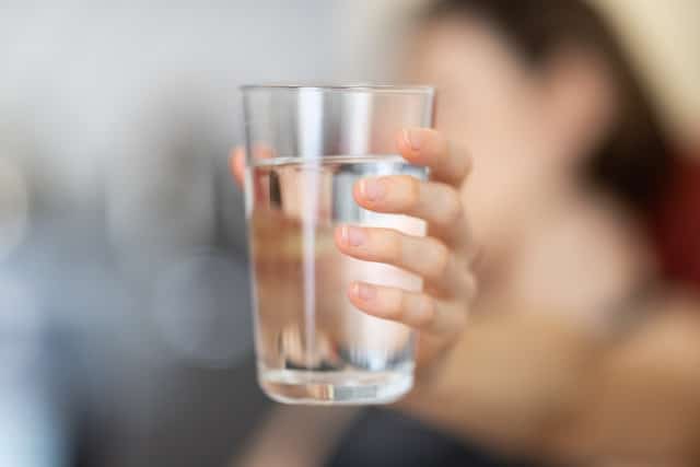 A photograph of a large clear glass tumbler of water held in someone's hand.