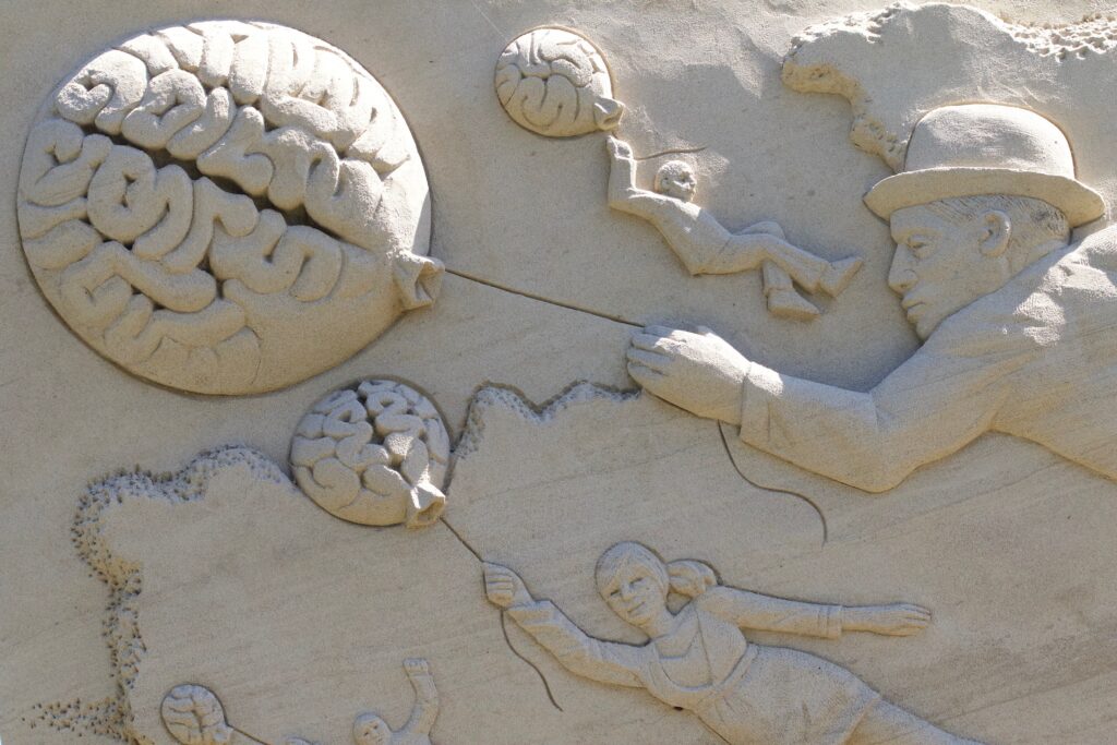 A cream-coloured sandy stone relief depicting a man in a hat, a woman and other people floating up into the clouds, all holding what appears to be brains-as-balloons, each on a string, pulling the holders up and away