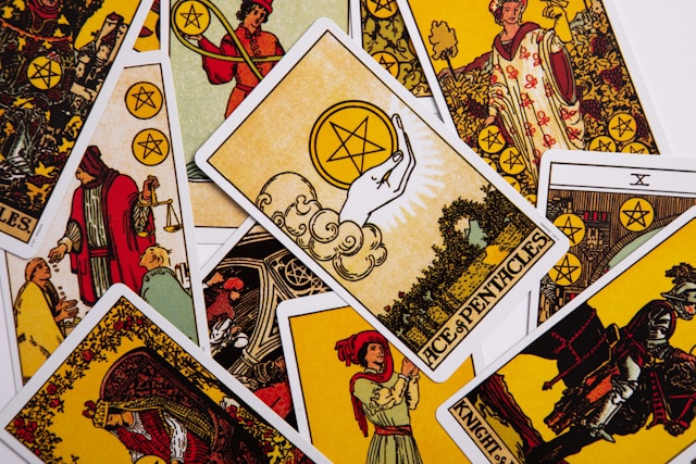 A photograph of several "Minor Arcana" cards from the Rider-Waite Tarot deck. Visible are the Ace of Pentacles - showing a hand holding a circle in which is a five-pointed star, Knight of pentacles, 10 of pentacles, and some other cards containing five-pointed stars but with the written values hidden by other cards. All are richly illustrated.