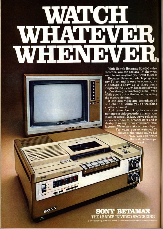 A magazine advert for Sony Betamax – The leader in video recording". A Sony Betamax video recorder stands in front of a Sony television set. Above these is "WATCH WHATEVER WHENEVER" in large block capitals. Smaller text reads "With Sony's Betamax SL-860 video recorder you can see any TV show you want to see anytime you want to see it. Because Betamax, which plugs into any TV set and is easy to operate, can videotape a show up to three hours long (with the L-750 videocassette) while you're doing something else – even while you're out of the the house, by setting the electronic timer. It can also videotape something off one channel while you're watching another channel And remember, Sony has more experience in videorecorders than anyone (over 20 years!) In fact we've sold more videorecorders to broadcasters and industry than any other consumer manufacturer, We even make our own tape. For years you've watched TV shows at times you've had to. Now you can watch them at the times you want to."