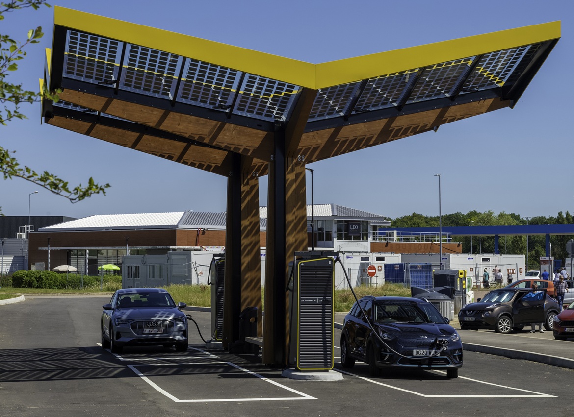 Photograph of an electric vehicle charging station, with four car spaces. Two cars are plugged in.