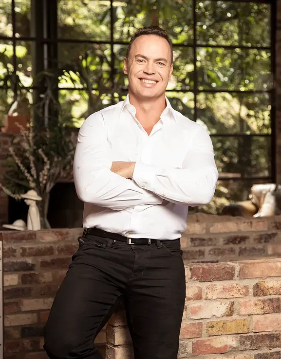 Photograph of a very clean-cut young man, standing with his arms crossed and a giant smile showing extremely white teeth.