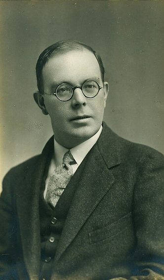 Black and white vintage portrait photograph of a bespectacled white man in a suit and tie.