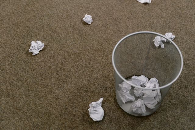 Photograph of balls of crumpled wastepaper in a wastepaper basket, and on the floor beside it.